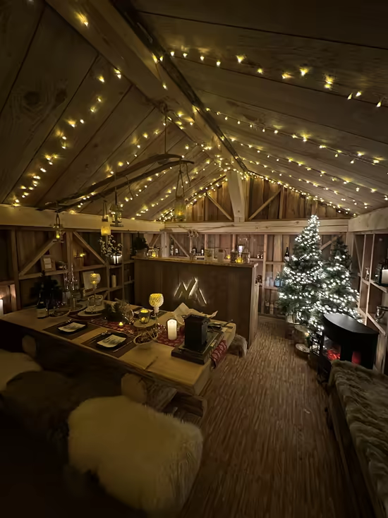A barn dressed for dinner: fairy lights under the beams, a Christmas tree and a set table