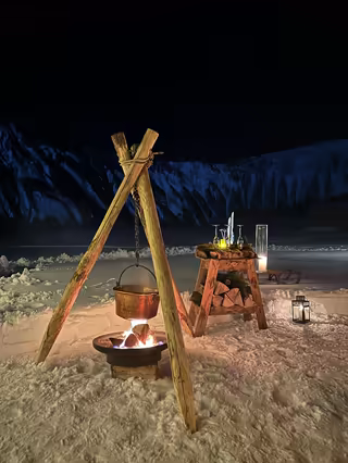 Cauldron over a campfire beside a champagne service, in the snow at night
