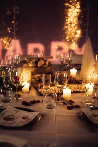 Candlelit table with rose petals before illuminated Marry Me letters and a curtain of golden lights