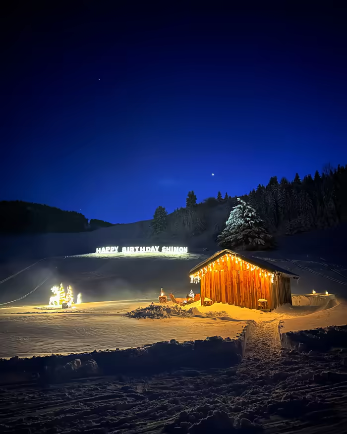 Small chalet strung with lights, an illuminated Happy Birthday sign at blue hour