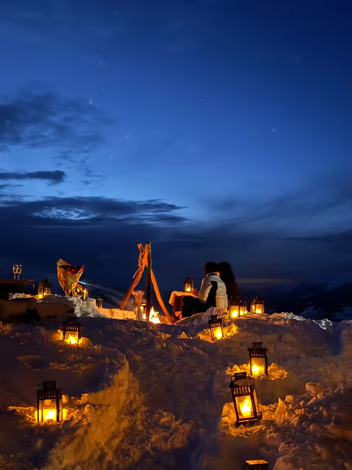 Couple by a campfire at blue hour, lanterns set into the snow