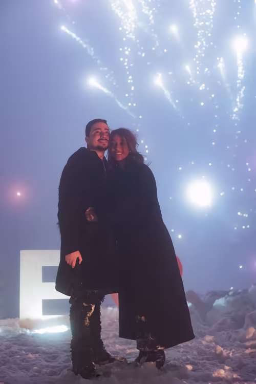 A couple embracing beneath fireworks, beside the lit letters