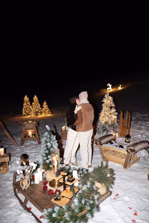A couple embracing among lit fir trees and lanterns, at night
