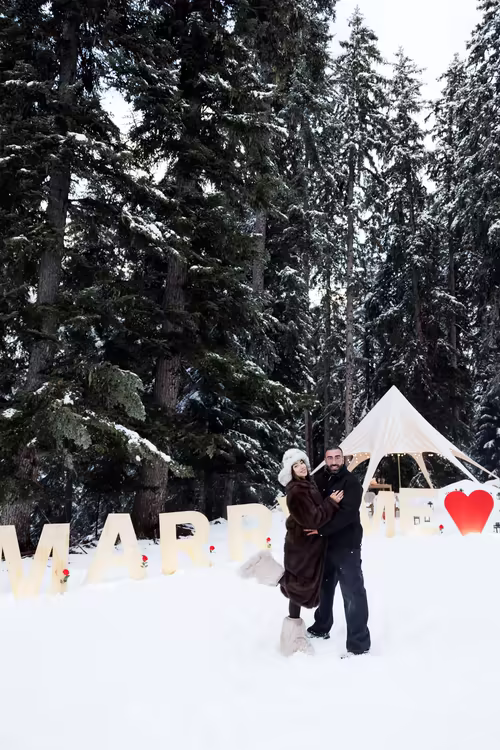 The couple among the Marry Me letters, the canopy and the forest behind them