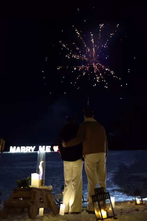 A couple seen from behind watching fireworks above the Marry Me letters