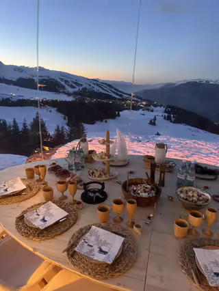 Table set inside a transparent bubble at sunset, facing the mountain panorama
