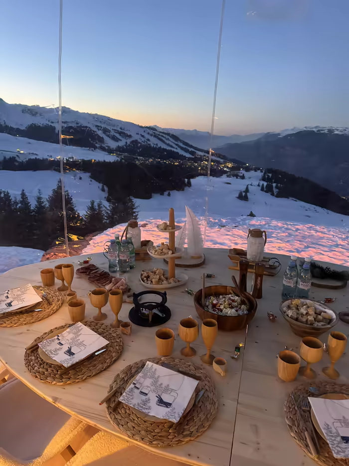 Table set inside a transparent bubble at sunset, facing the mountain panorama