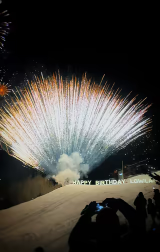 Fireworks over an illuminated Happy Birthday sign, guests filming from the snow