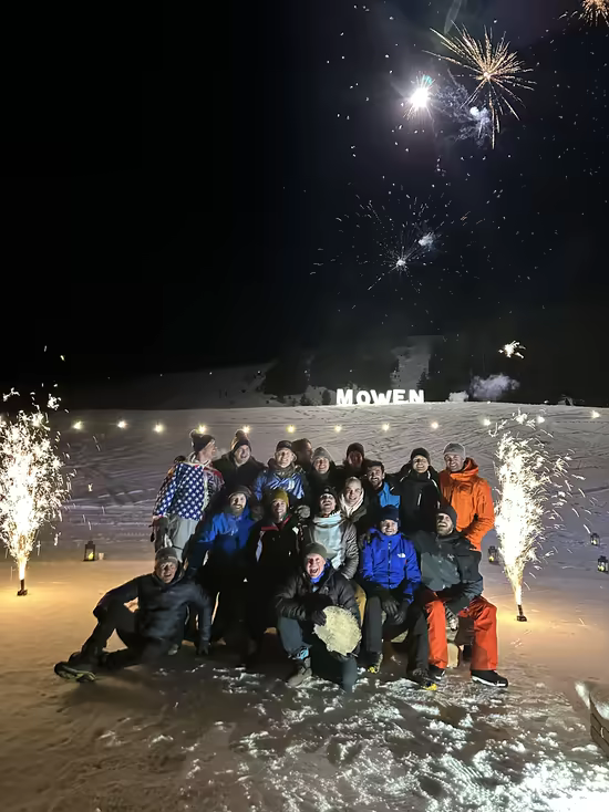 A group gathered in the snow under fireworks, sparkling fountains on each side and a name in lights
