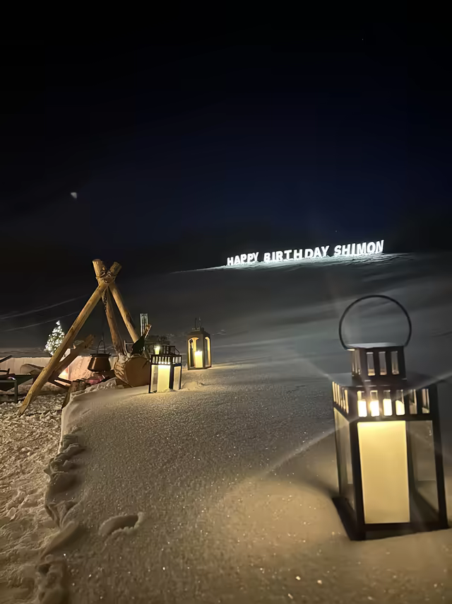Illuminated Happy Birthday letters on a snowy slope, lined with lanterns