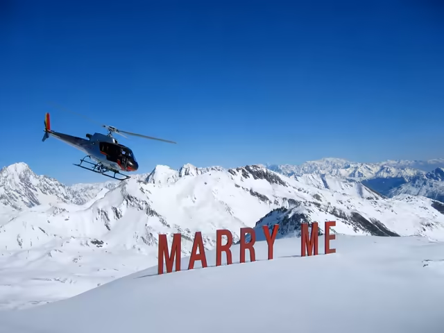Helicopter over giant red Marry Me letters in the snow, among the peaks of the French Alps