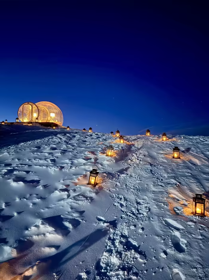 Lantern-lined path through the snow to two lit bubbles, blue hour in the 3 Vallées