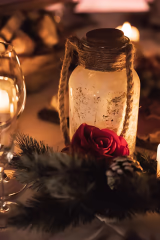 A lantern, a red rose and a pine cone on a table set for a winter dinner