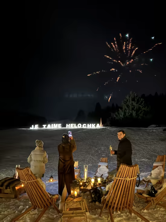 Fireworks above a lit love message, guests on deck chairs around the fire