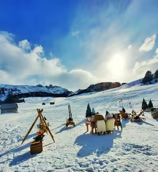 Picnic on the snow with sleighs, fur-covered chairs and a campfire, in the sun of the 3 Vallées