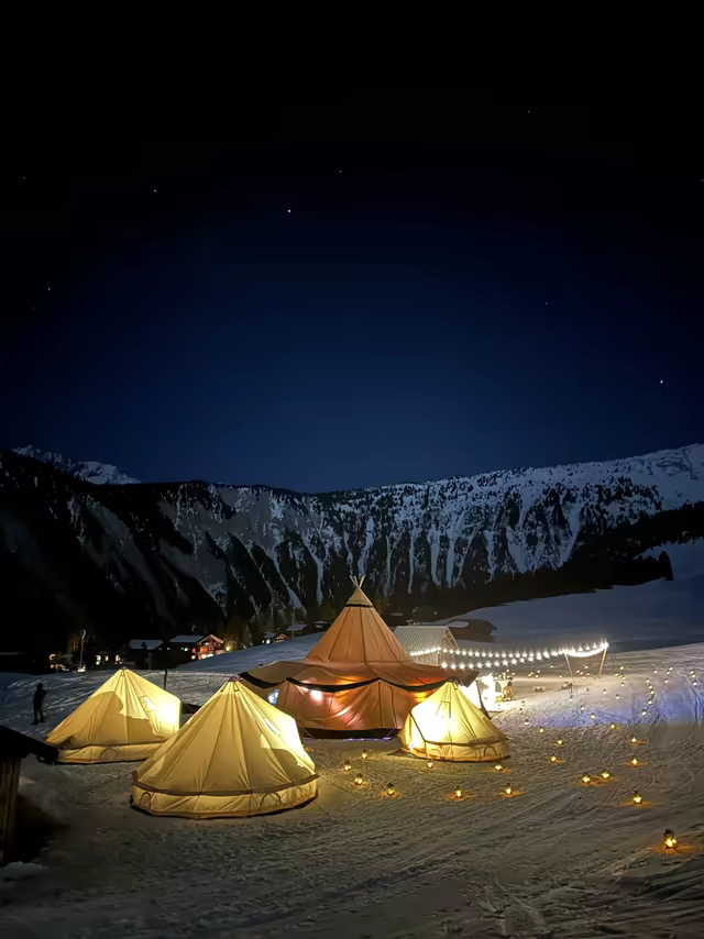 Tents glowing on a snowy slope under a starry sky, in Savoie