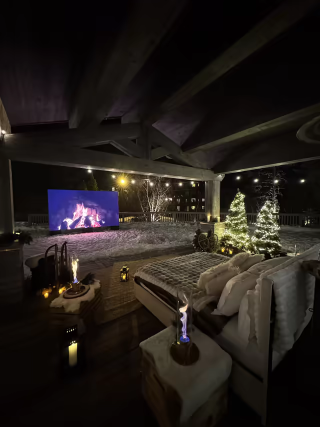 Snowy terrace lounge with a fireplace screen, a Christmas tree and flame lamps, at night