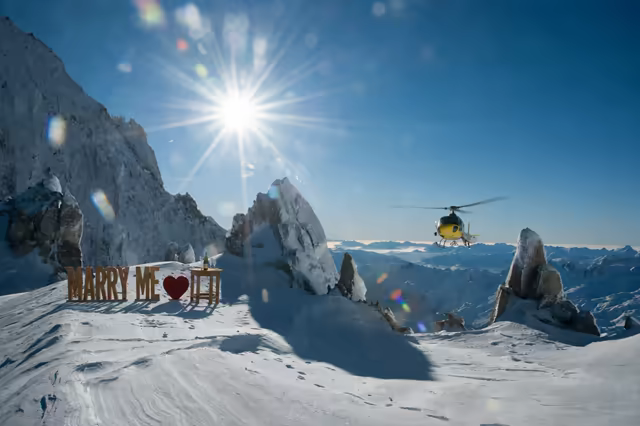 Marry Me letters on a snowy summit of the French Alps, a helicopter passing in the sun