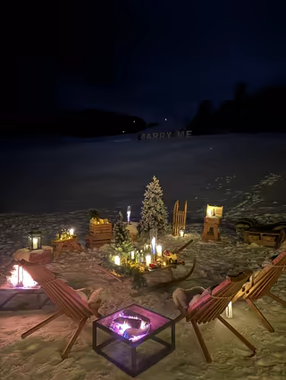 Proposal setting of illuminated Marry Me letters, fire pits, deck chairs and candles in the snow