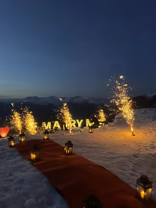 Red carpet lined with lanterns towards illuminated Marry Me letters and sparklers, at dusk
