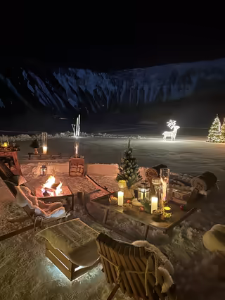 Fire pit, candles and champagne on fresh snow, among lit reindeer and fir trees