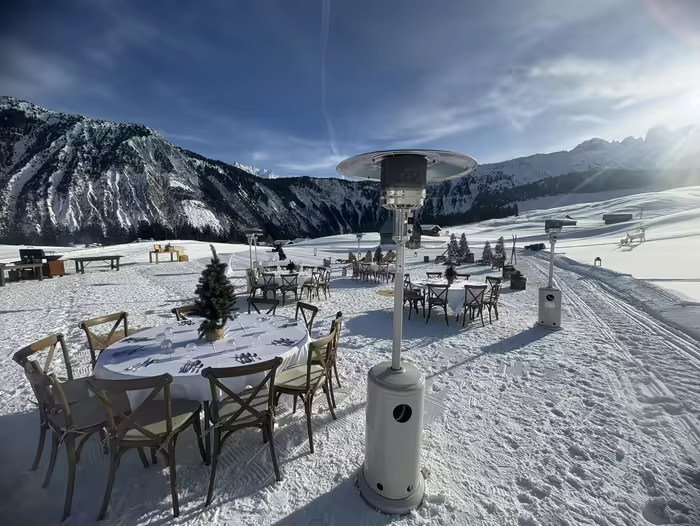 Round tables and patio heaters set out on the snow for a daytime reception, the mountains behind