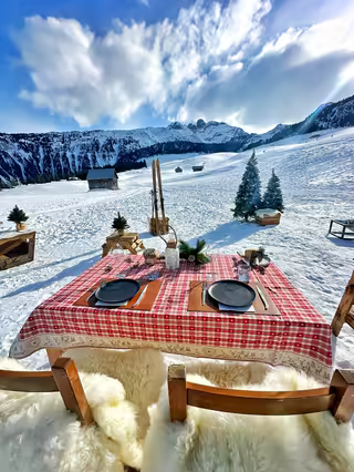 Table for two with a checked cloth and sheepskins, in the snow of the 3 Vallées