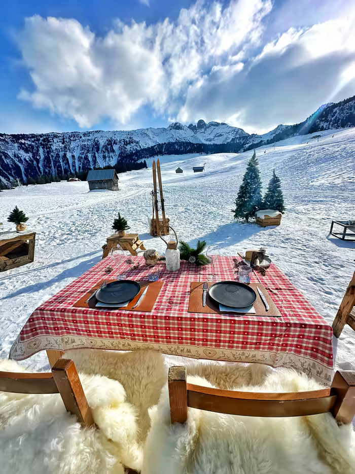 Table for two with a checked cloth and sheepskins, in the snow of the 3 Vallées