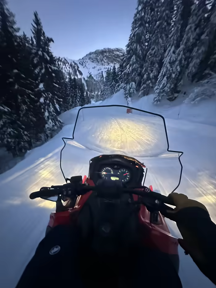 Snowmobile rider’s view down a forest track at dusk, above Courchevel
