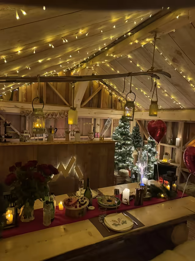 Table of red roses and candles under fairy lights in a wooden barn, a heart balloon above