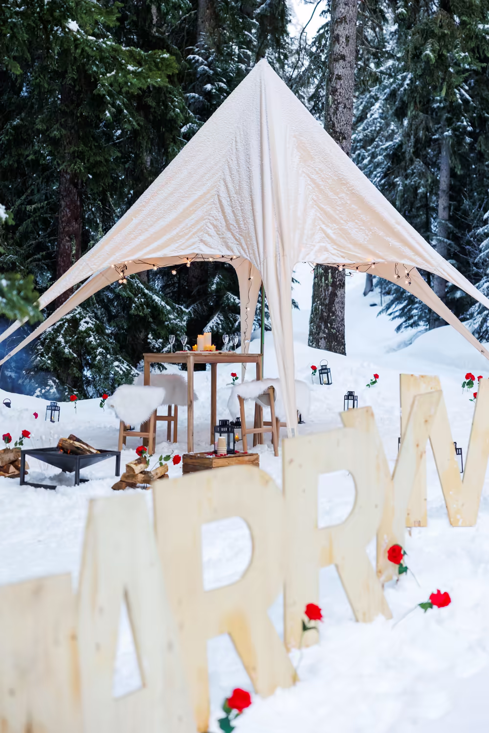 Wooden Marry Me letters dotted with roses in front of the white canopy, in a forest clearing